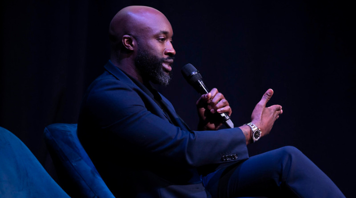 Man holding a mic while sitting in a chair 